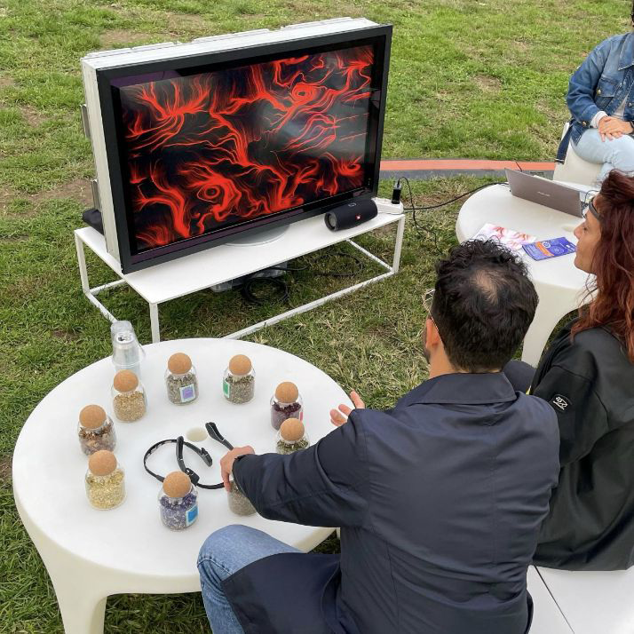 Partecipanti annusano fragranze durante una sessione BrainArt® all'aperto: l'opera visiva rossa generata dalle onde cerebrali appare sul monitor
