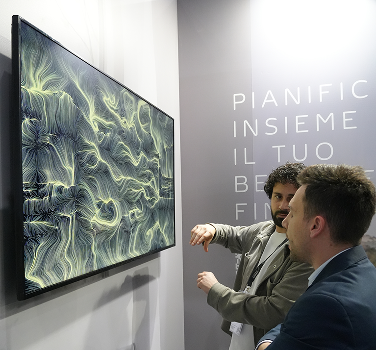 Operatore BrainArt® spiega a un visitatore un'opera visiva generativa su monitor durante una fiera