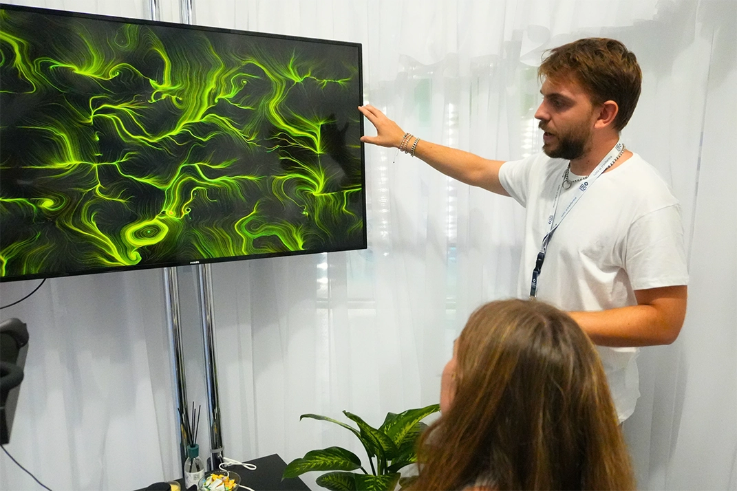 Operatore BrainArt® illustra a una partecipante l'opera visiva verde generata dalle sue onde cerebrali su monitor