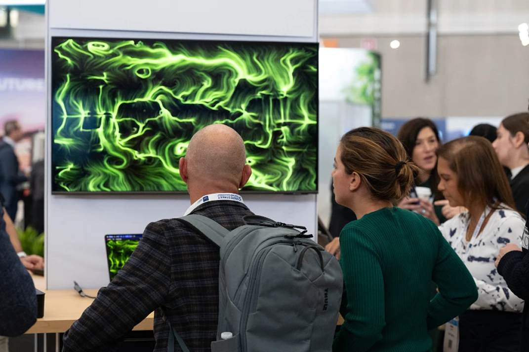 Visitatori di una fiera osservano un'opera BrainArt® verde generata da onde cerebrali su grande schermo allo stand