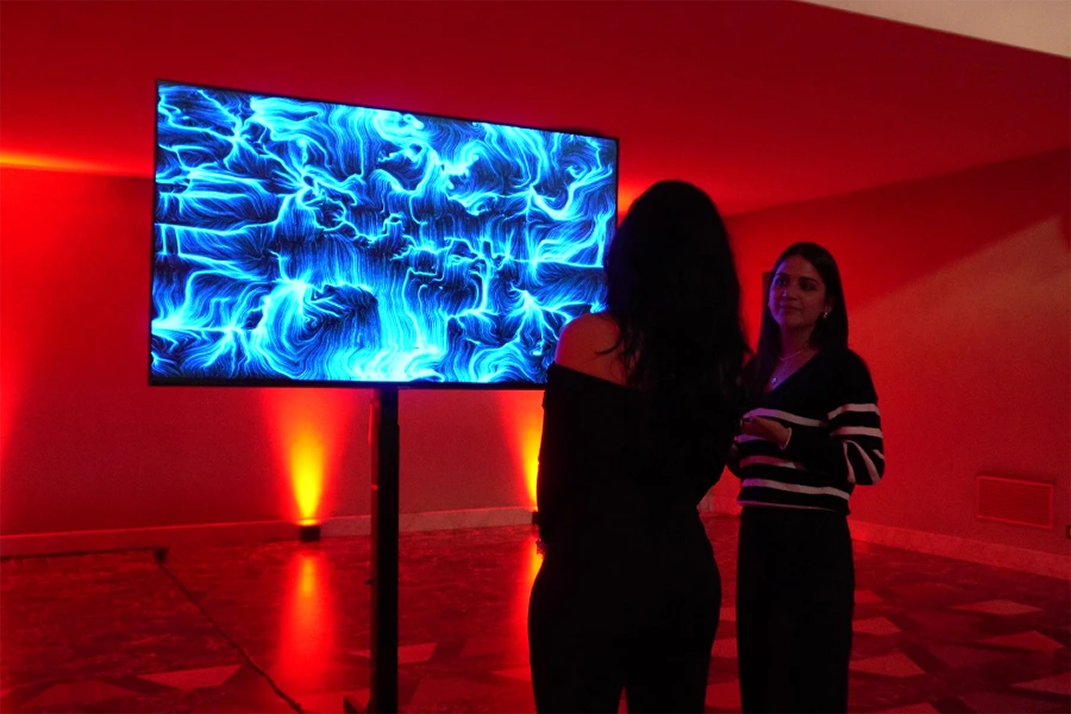 Operatrice BrainArt® spiega a una partecipante l'opera visiva blu generata da onde cerebrali su grande schermo durante un evento serale